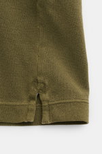 Stone Island Poloshirt oliv aus Baumwoll-Piqué, Slim Fit, seitliche Saumschlitze, Detailaufnahme vom unteren Saum mit strukturierter Oberfläche.