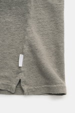 Close-up bottom side view of 04651/ A trip in a bag Linen jersey polo shirt grey-green showing slightly elasticated linen fabric, slim fit hem with short vents, and a small woven label in the side seam. 

<p>This casual, piece-dyed jersey polo shirt from 