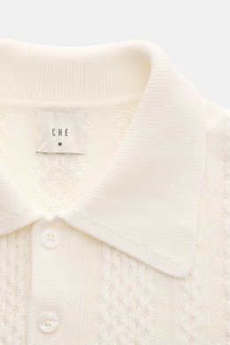 Nahaufnahme des Ché Kurzarm-Strickpolo 'Santino' creme von oben, zeigt grobes, asymmetrisches Strickmuster, Polokragen, Drei-Knopf-Leiste, Baumwolle, Regular Fit, flexible Rippbündchen und tonales CHÉ-Weblabel.
