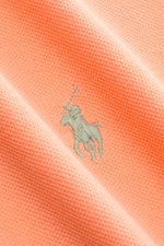Nahaufnahme des orangefarbenen Polo Ralph Lauren Poloshirts mit ikonischem Poloreiter-Stitching, Piqué-Struktur aus reiner Baumwolle.