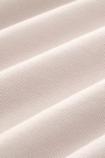 Nahaufnahme des 04651/ A trip in a bag Poloshirt 'Johnny' sand aus Piqué-Baumwolle mit offener Kragenleiste, Regular Fit, Ärmelbündchen, Saumschlitzen und kleinem Weblabel, detailreich von schräger Seite fotografiert.