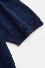 Nahaufnahme des Ärmels und Saums des 04651/ A trip in a bag Kurzarm-Strickpolo 'Hansen' navy, mit feinem Jacquard-Muster, klassischem Polokragen, Oversized Fit, aus Leinen-Baumwoll-Mix mit leicht griffiger Haptik, fotografiert von oben auf weißen Hintergr