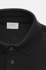 Nahaufnahme des schwarzen 04651/ A trip in a bag Poloshirts 'Wool TP' in Slim Fit, von oben fotografiert, Piqué aus Baumwolle und Wolle, weicher Griff, klassischer Polokragen, glatte Drei-Knopf-Leiste, kleines Weblabel in der Seitennaht, komfortable Rippb