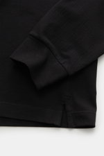 Close-up photo of the sleeve and hem from the side of the Stone Island Longsleeve-Poloshirt schwarz in black, showing its garment dyed, grippy piqué cotton fabric with elastic quality, slim fit, and short side slits. Legere Kombinationen gelingen mit dies