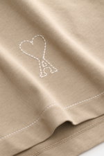 Close-up view of Ami Paris Jersey long sleeve polo shirt taupe fabric showing signature logo stitching, soft pure cotton jersey with oversized fit, dress-shirt collar, and three-button patch placket. Contemporary and casual: With its generous oversized fi