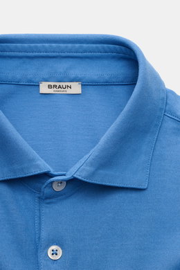 Nahaufnahme des blauen BRAUN Hamburg Jersey Longsleeve-Poloshirts aus reiner Baumwolle mit Haifisch-Polokragen, glatter Drei-Knopf-Leiste, Slim Fit und seitlichen Saumschlitzen, fotografiert von oben.