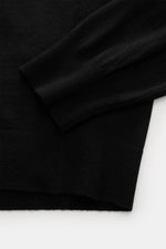 Close-up top-down view of the von Braun Merino knit polo black sleeve and hem, showing soft pure merino wool with elasticated ribbed bands.