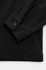 Nahaufnahme von Ärmel und Saum des Stone Island Longsleeve Jersey-Poloshirt 'Ghost Piece' schwarz aus leicht geflammtem Baumwolljersey mit tonalem STONE ISLAND-Weblabel und klassischer Sportmanschette, fotografiert von oben.