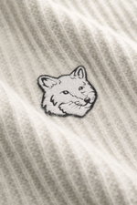 Nahaufnahme aus schräger Perspektive des Maison Kitsuné Strickpolo 'Fox Head' sand mit tonalem Fuchs-Stitching, reiner Wolle, weichem Griff, breitem Rippstrick, mittelfeinem Strickbild, Regular Fit, gestricktem Polokragen, Drei-Knopf-Leiste und komfortabl