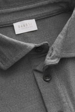 Nahaufnahme aus schräger Draufsicht auf den Kragen und das Label des 04651/ A trip in a bag Longsleeve-Poloshirt 'WJ' grau meliert mit Mix aus Wolle und hochwertiger Microfaser, weichem Griff, Regular Fit, klassischem Polokragen und kurzen Saumschlitzen.