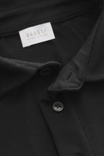 Close-up top-down view of the black 04651/ A trip in a bag Longsleeve polo shirt 'WJ' black showing collar, button, and label, blend of wool and microfiber, soft touch, regular fit, classic polo collar, short hem slits.