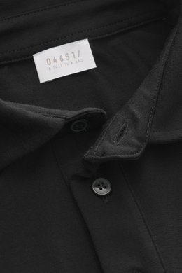 Close-up top-down view of the black 04651/ A trip in a bag Longsleeve polo shirt 'WJ' black showing collar, button, and label, blend of wool and microfiber, soft touch, regular fit, classic polo collar, short hem slits.