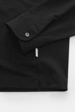 Close-up front view of the black 04651/ A trip in a bag Longsleeve polo shirt 'WJ' black showing the cuff with button, made from a blend of wool and high-quality microfiber, soft touch, regular fit, classic polo collar, and short hem slits.