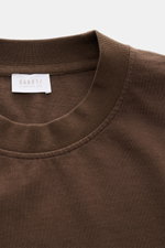 Close-up top view of the brown 04651/ A trip in a bag Rundhals-T-Shirt 'Nunu Tee' showing the ribbed round neckline and fabric texture. <p>Tauchen Sie ein in den relaxten Lifestyle von 04651/ A TRIP IN A BAG – das unkomplizierte 'Nunu Tee' aus hochwertige