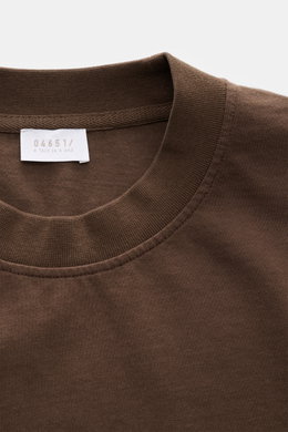 Close-up top view of the brown 04651/ A trip in a bag Rundhals-T-Shirt 'Nunu Tee' showing the ribbed round neckline and fabric texture. <p>Tauchen Sie ein in den relaxten Lifestyle von 04651/ A TRIP IN A BAG – das unkomplizierte 'Nunu Tee' aus hochwertige
