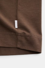 Close-up of the hem and side seam of the brown 04651/ A trip in a bag Rundhals-T-Shirt 'Nunu Tee' braun, photographed from a front angle, showing the white web label. <p>Tauchen Sie ein in den relaxten Lifestyle von 04651/ A TRIP IN A BAG – das unkomplizi