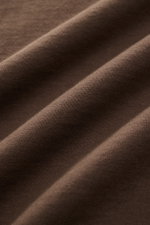 Close-up fabric detail of the brown 04651/ A trip in a bag Rundhals-T-Shirt 'Nunu Tee' showing soft, medium-weight pure cotton jersey from a side angle. <p>Tauchen Sie ein in den relaxten Lifestyle von 04651/ A TRIP IN A BAG – das unkomplizierte 'Nunu Tee