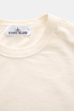 Stone Island Rundhals-T-Shirt 'Marina' creme, nah von oben fotografiert, reine Baumwolle, weicher Griff, schwere Qualität, Oversized Fit, Rundhalsausschnitt, kontrastfarbenes Rippstrick-Detail auf der Schulter, dezenter Logo-Print auf der Front.