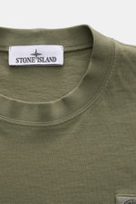 Nahaufnahme des olivfarbenen Stone Island T-Shirts 'Dyed Regular Fit' von oben, aus reiner Baumwolle mit Rundhalsausschnitt, weichem Griff und Weblabel auf der Brust.