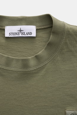Nahaufnahme des olivfarbenen Stone Island T-Shirts 'Dyed Regular Fit' von oben, aus reiner Baumwolle mit Rundhalsausschnitt, weichem Griff und Weblabel auf der Brust.