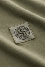 Nahaufnahme des Weblabels auf der Brust des Stone Island T-Shirts 'Dyed Regular Fit' oliv aus reiner Baumwolle mit weichem Griff.
