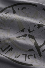 Nahaufnahme des plakativen Rückenprints auf dem Stone Island Rundhals-T-Shirt dunkelgrau, aufgenommen aus schräger Perspektive. Markantes Casual-Basic aus schwerer Baumwollqualität mit weichem Griff, Regular Fit, Rundhalsausschnitt und STONE ISLAND-Print 