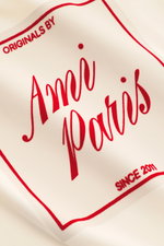 Nahaufnahme des Ami Paris Rundhals-T-Shirt creme, gefertigt aus reiner Baumwolle mit geflocktem roten AMI PARIS-Schriftzug frontal, weicher Griff, Regular Fit, Rundhalsausschnitt und rückwärtigem Logo-Stitching.