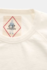 Nahaufnahme des C.P. Company Rundhals-Kurzarm-Sweatshirts creme von oben, leichte Baumwolle, Raglanärmel, Rippbündchen, Logo-Print innen.