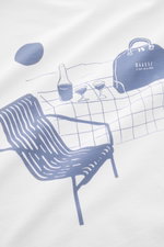 Close-up of the back print on the 04651/ A trip in a bag T-Shirt 'Nunu' white, photographed from above, showing a minimalist blue illustration of a chair, table with bottle and two glasses, and a bag with the brand logo.

<p>A basic with a print accent: W