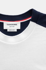 Nahaufnahme des Thom Browne T-shirts weiß/schwarz von oben, reine Baumwolle, weicher Griff, slim fit, Rundhalsausschnitt, Brusttasche, kontrastfarbene Streifen am Arm, kurze Saumschlitze, verlängerte Rückseite.