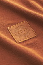 Close-up front view of the rust brown Stone Island Crew Neck T-Shirt 'Ghost Piece' showing smooth cotton jersey texture and tonal woven label on the chest.

<p>With this crew neck T-shirt made of smooth cotton jersey, featuring a tonal woven label on the 