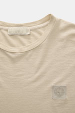 Stone Island Crew Neck T-Shirt 'Ghost Piece' beige shown from front close-up, smooth cotton jersey with tonal woven label on chest.  
<p>With the crew neck T-shirt made of smooth cotton jersey, featuring a tonal woven label on the chest, STONE ISLAND deli