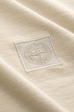 Close-up front angle of Stone Island Crew Neck T-Shirt 'Ghost Piece' beige showing tonal woven label on smooth cotton jersey fabric.

Description: <p>With the crew neck T-shirt made of smooth cotton jersey, featuring a tonal woven label on the chest, STON