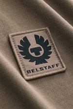 Nahaufnahme des Belstaff Rundhals-T-Shirts taupe, Fokus auf das dezente Weblabel aus Baumwoll-Jersey mit weichem Griff, Slim Fit, aus schräger Perspektive.