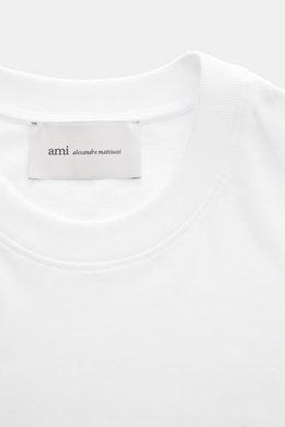 Ami Paris Crew Neck T-Shirt white shown from a close-up top-front view, featuring a pure cotton jersey, soft touch, slim fit, crew neckline, heart stitching on chest, and tonal AMI stitching on back. Classic jersey basic by the French label AMI PARIS: Thi