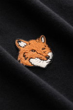 Close-up front view of Maison Kitsuné Crew Neck T-Shirt 'Fox Head' black showing an embroidered orange fox patch on soft, black pure cotton fabric.

<p>Sporty essential from MAISON KITSUNÉ: With the typical fox patch on the chest, this shirt will be a fav