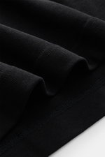 Close-up view of folded fabric showing texture and stitching details of Jacquemus Crew Neck T-Shirt Black, pure cotton, soft touch, slim fit, with grosgrain and logo stitching on the chest.