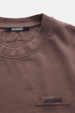 Close-up front view of Jacquemus Crew Neck T-Shirt Grey Brown showing pure cotton fabric, soft touch, slim fit, and Grosgrain with logo stitching on the chest.