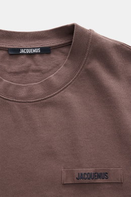 Close-up front view of Jacquemus Crew Neck T-Shirt Grey Brown showing pure cotton fabric, soft touch, slim fit, and Grosgrain with logo stitching on the chest.