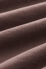 Close-up of Jacquemus Crew Neck T-Shirt Grey Brown fabric showing texture and folds, photographed from a side angle; pure cotton, soft touch, slim fit, Grosgrain with logo stitching on the chest.