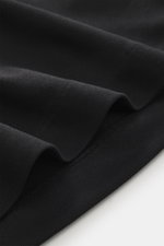 Close-up detail of black fabric folds showing texture and stitching, photographed from above, highlighting the Jacquemus Crew neck T-Shirt 'Rond Carre' black made of a mix of paper and microfiber with a matte look, regular fit, logo stitching on the side 