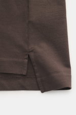 Close-up side view of Jacquemus Crew neck T-shirt 'Le Montaigne MC' dark brown, showing jersey made of pure cotton with soft touch, fine diagonal texture, slim fit, crew neckline, woven label on chest, side hem slits, and extended back.