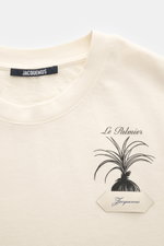 Close-up front view of Jacquemus Crew Neck T-Shirt cream showing neckline and chest with black palm print, grosgrain logo stitching, pure cotton, soft touch, slim fit.
