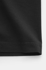 Close-up image of the hem of the Maison Kitsuné Crew neck T-Shirt black, photographed from a side perspective, showing pure cotton fabric with a slightly textured feel, regular fit, boxy cut, crew neckline, and distinctive fox print on the chest.