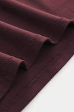 Close-up view of burgundy fabric folds showing stitching detail of the Kiefermann Crew neck T-shirt 'Hero' burgundy, with a blend of cotton and modal, elasticated fabric, soft touch, slim fit, and crew neck.