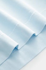Close-up of the pastel blue fabric folds of the 04651/ A trip in a bag Crew neck T-Shirt, showing heavy cotton jersey texture from a top-down perspective. Durable basic: This crew neck T-shirt from 04651/ A TRIP IN A BAG is made from heavy cotton jersey, 