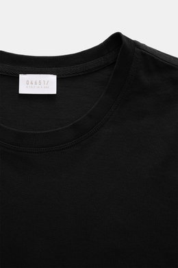 Close-up front view of the neckline and label of the 04651/ A trip in a bag Longsleeve 'Jersey Tee' black, made of light cotton jersey with a soft feel, regular fit, light quality, round neckline, and short hem slits. Versatile basic for comfortable layer