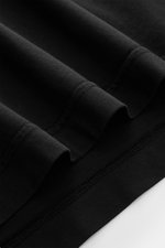 Close-up angled view of the 04651/ A trip in a bag Longsleeve 'Jersey Tee' black showing light cotton jersey fabric with soft feel, regular fit, round neckline, and short hem slits.