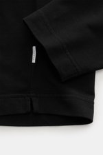 Nahaufnahme des schwarzen 04651/ A trip in a bag Longsleeve 'IF Tee' mit Saumschlitzen und Label, von oben fotografiert, Jersey aus elastischer Baumwolle, soft und Regular Fit.