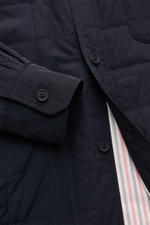 Nahaufnahme der Thom Browne Daunenjacke navy von schräg oben, zeigt leichte Daunenfüllung, Steppung, Knopfleiste, Manschette und gestreiftes Innenfutter.